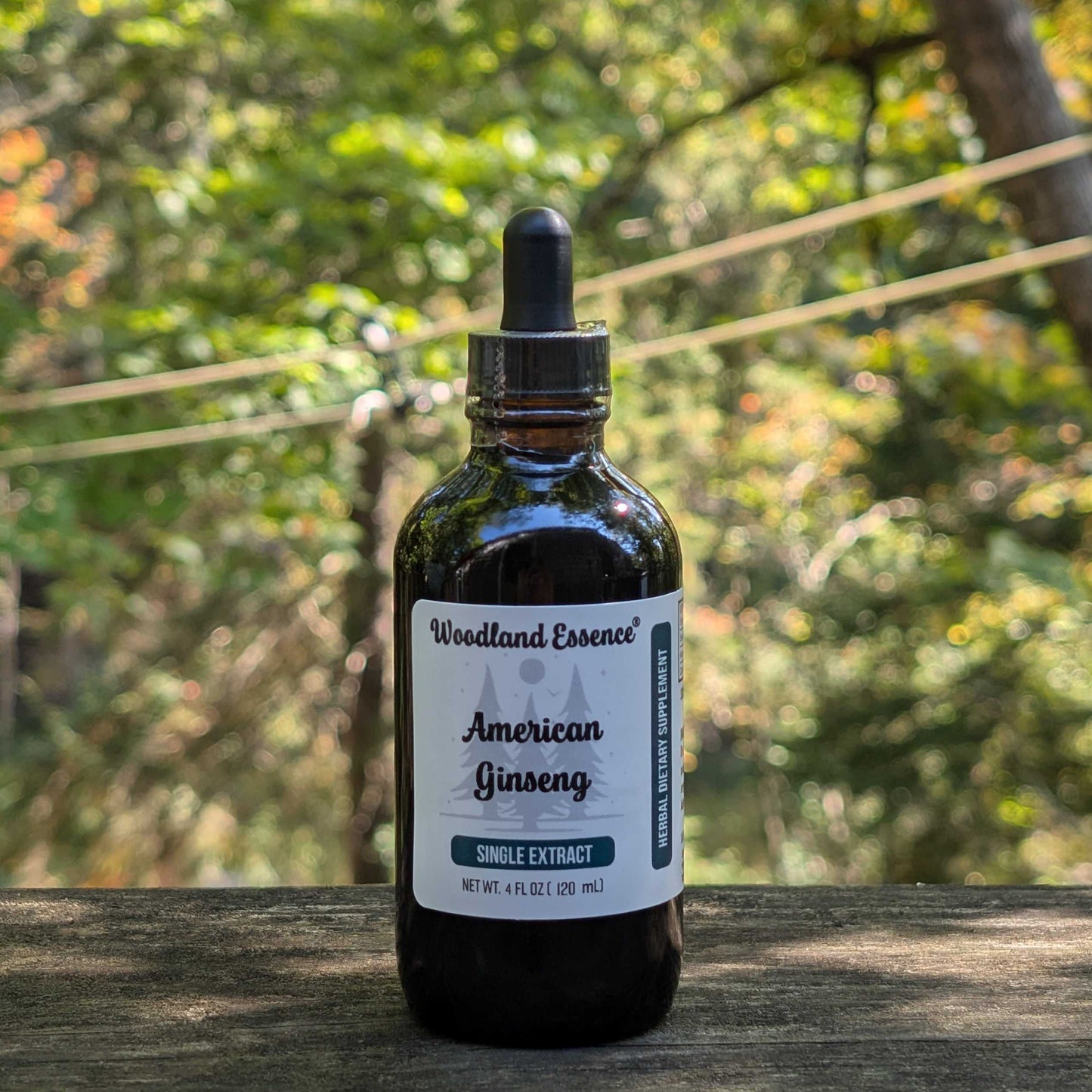 Bottle of Woodland Essence American Ginseng extract on a wooden surface with a forest background