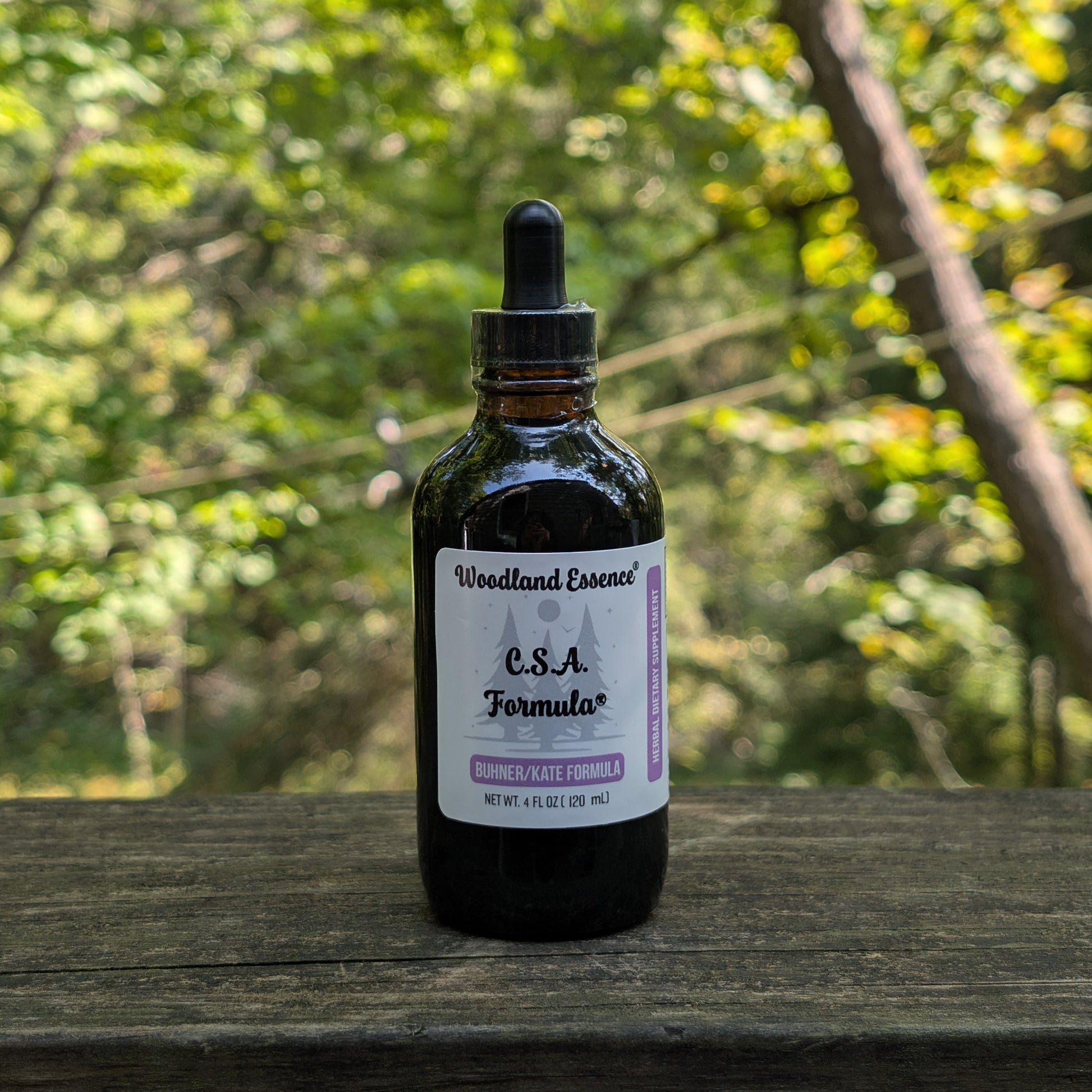 Bottle of Woodland Essence C.S.A. Formula on a wooden surface with a blurred natural background