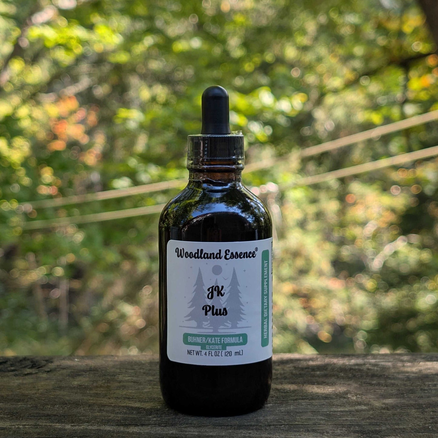 Bottle of Woodland Essence JK Plus tincture on a wooden surface with a blurred green natural background