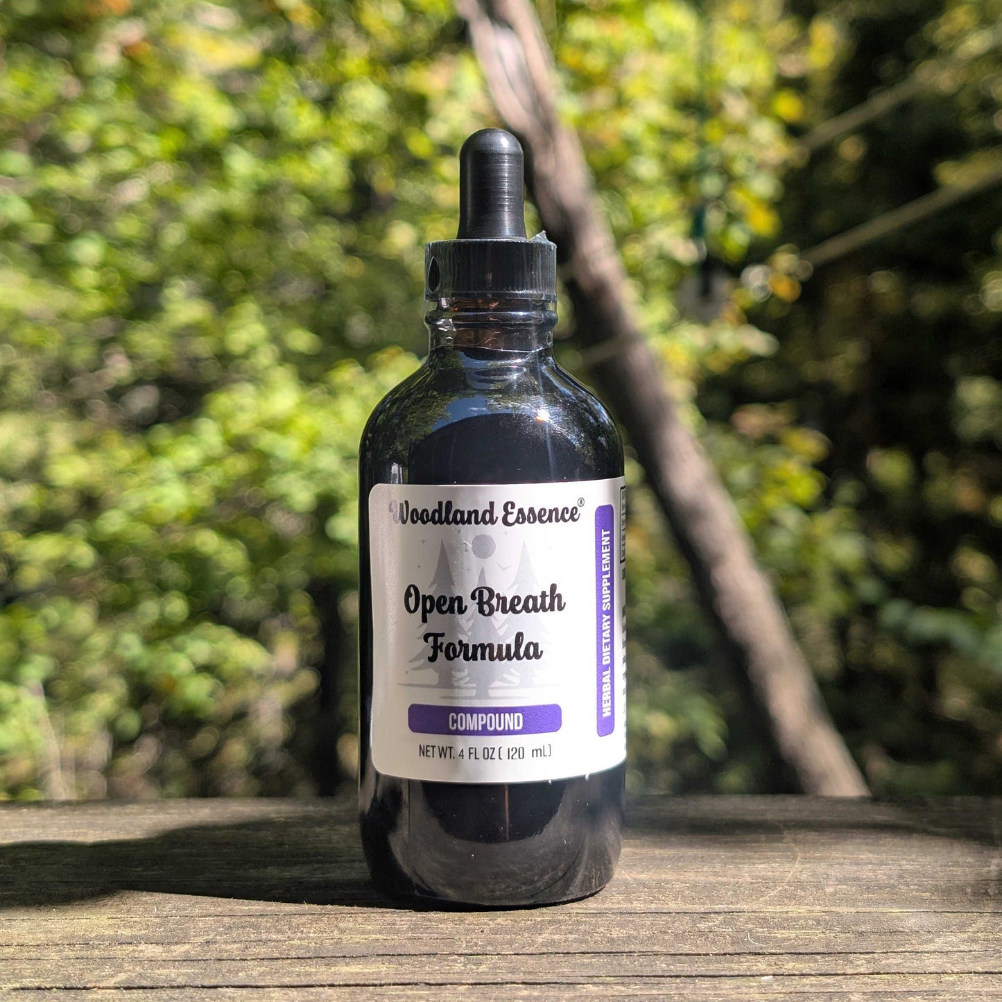 Bottle of Woodland Essence Open Breath Formula Compound on a wooden surface with a blurred natural background
