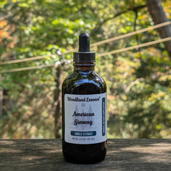Bottle of Woodland Essence American Ginseng extract on a wooden surface with a forest background