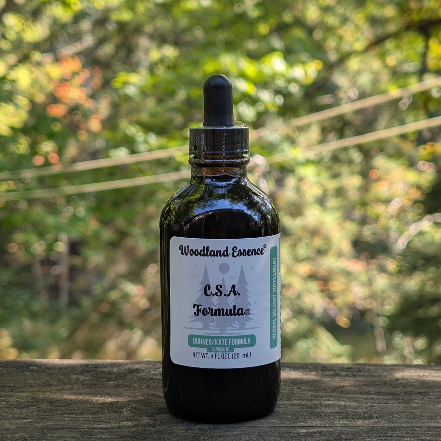 Bottle of Woodland Essence C.S.A. Formula on a wooden surface with a blurred natural background