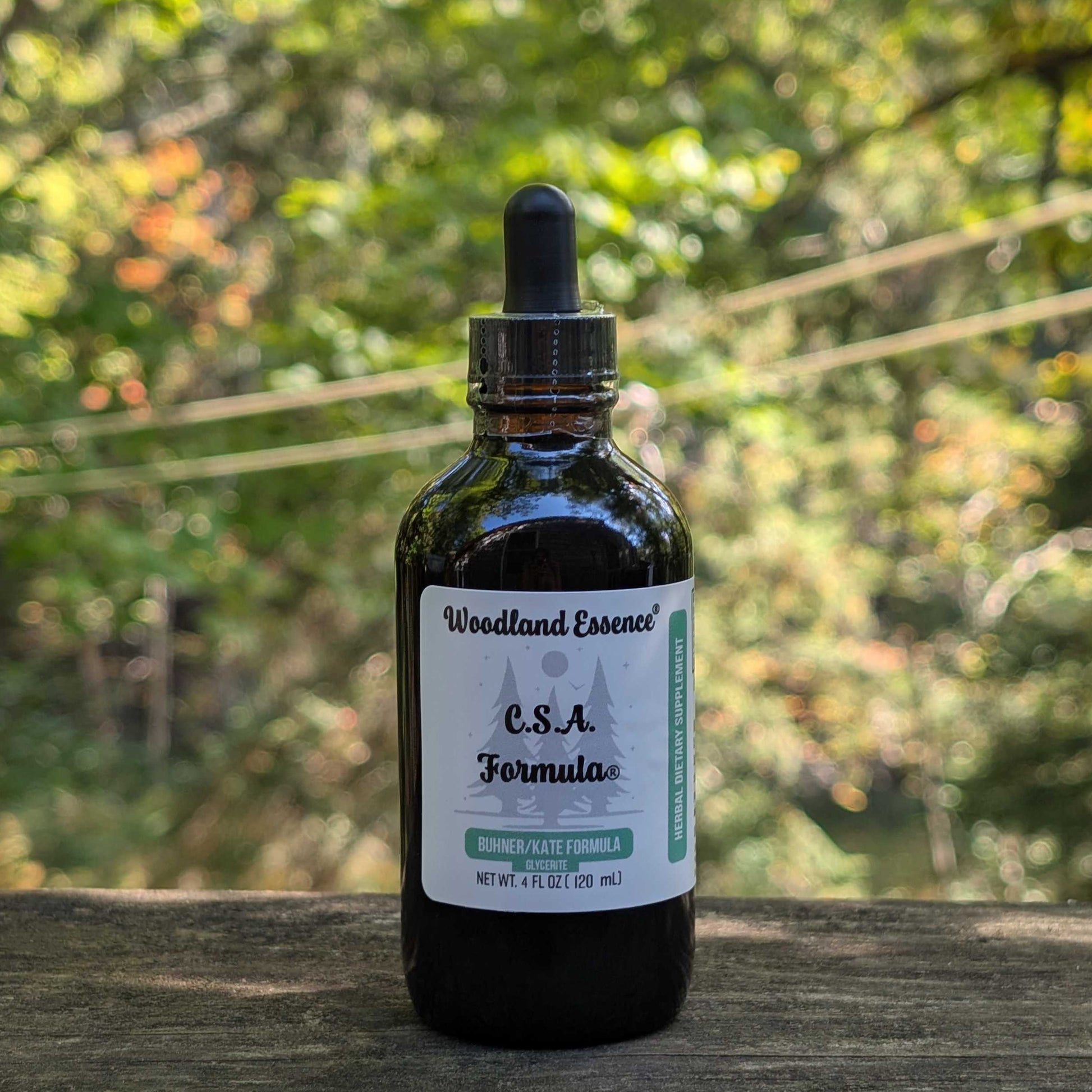 Bottle of Woodland Essence C.S.A. Formula on a wooden surface with a blurred natural background
