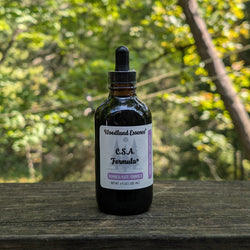 Bottle of Woodland Essence C.S.A. Formula on a wooden surface with a blurred natural background
