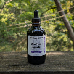 Bottle of 'Clear Focus Formula' from 'Woodland Essence' on a wooden surface with a natural background.