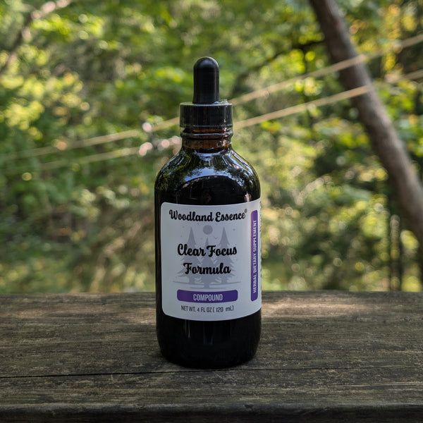 Bottle of 'Clear Focus Formula' from 'Woodland Essence' on a wooden surface with a natural background.