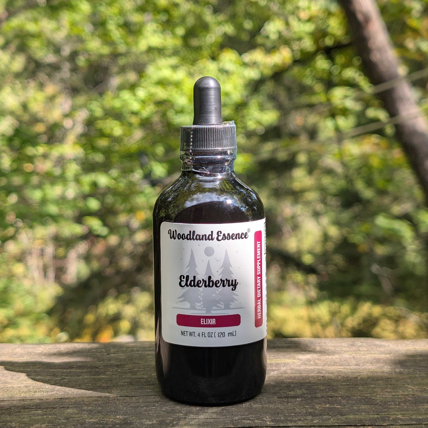 Bottle of Woodland Essence Elderberry Elixir on a wooden surface with a blurred natural background