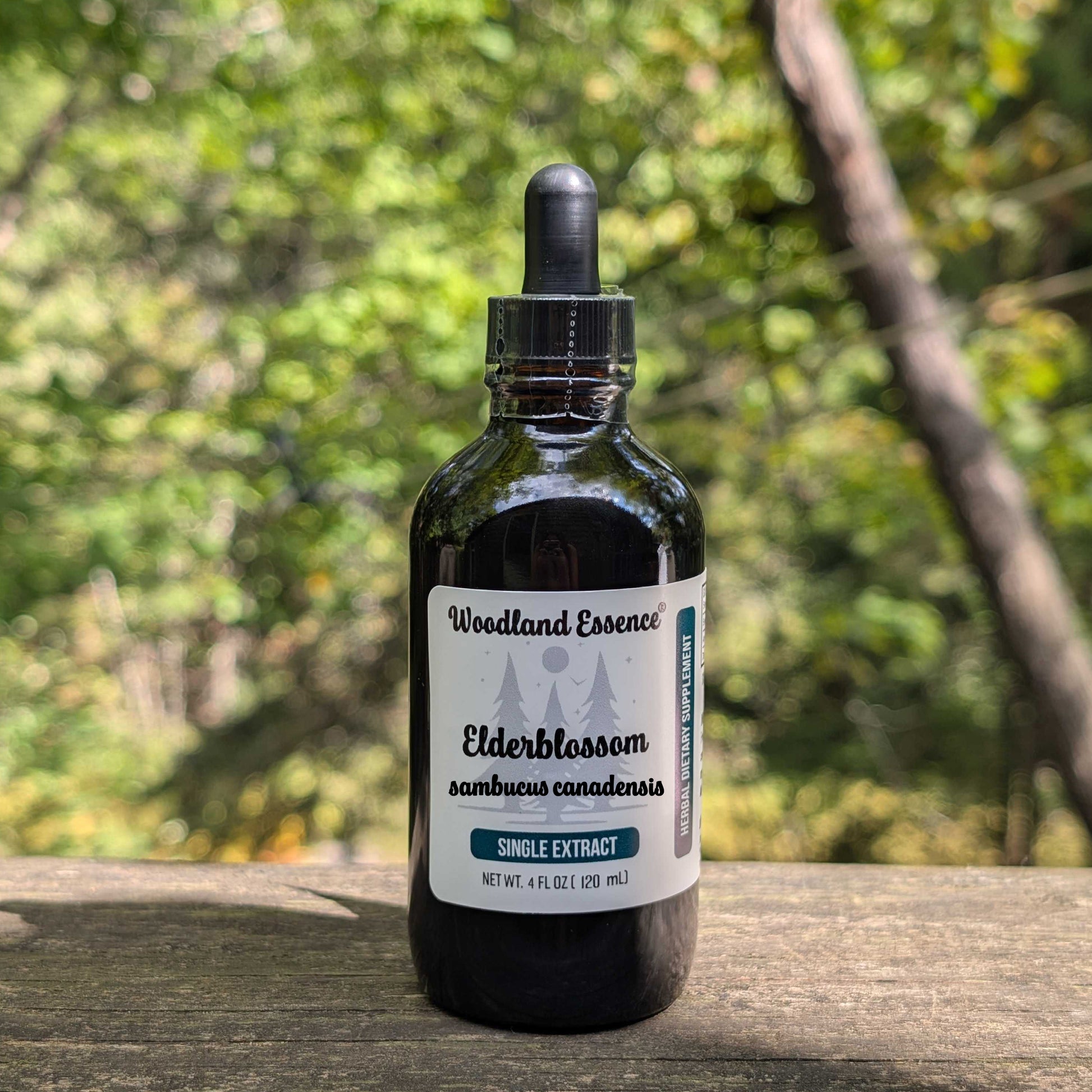 Bottle of Woodland Essence Elderblossom extract on a wooden surface with a blurred natural background