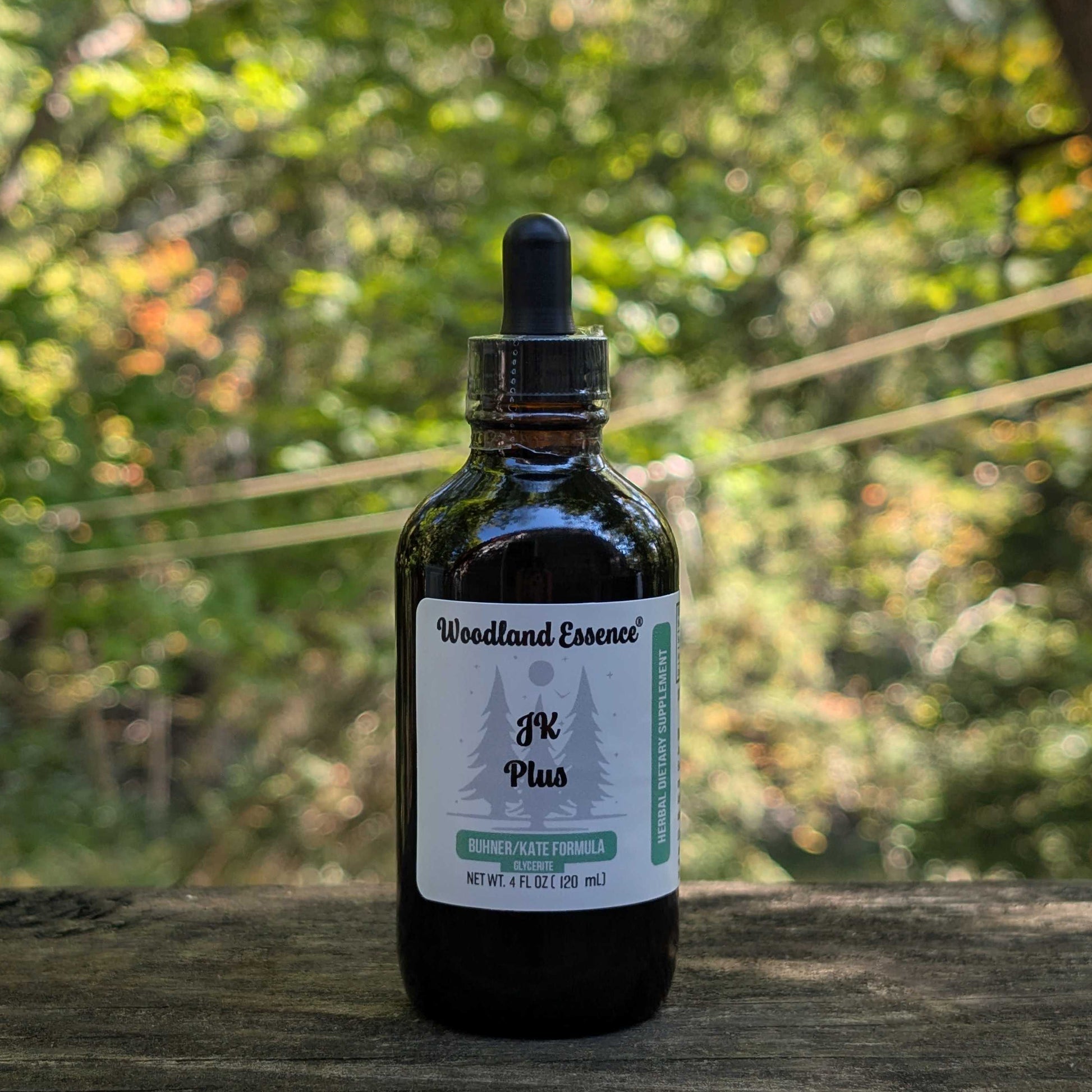 Bottle of Woodland Essence JK Plus tincture on a wooden surface with a blurred green natural background