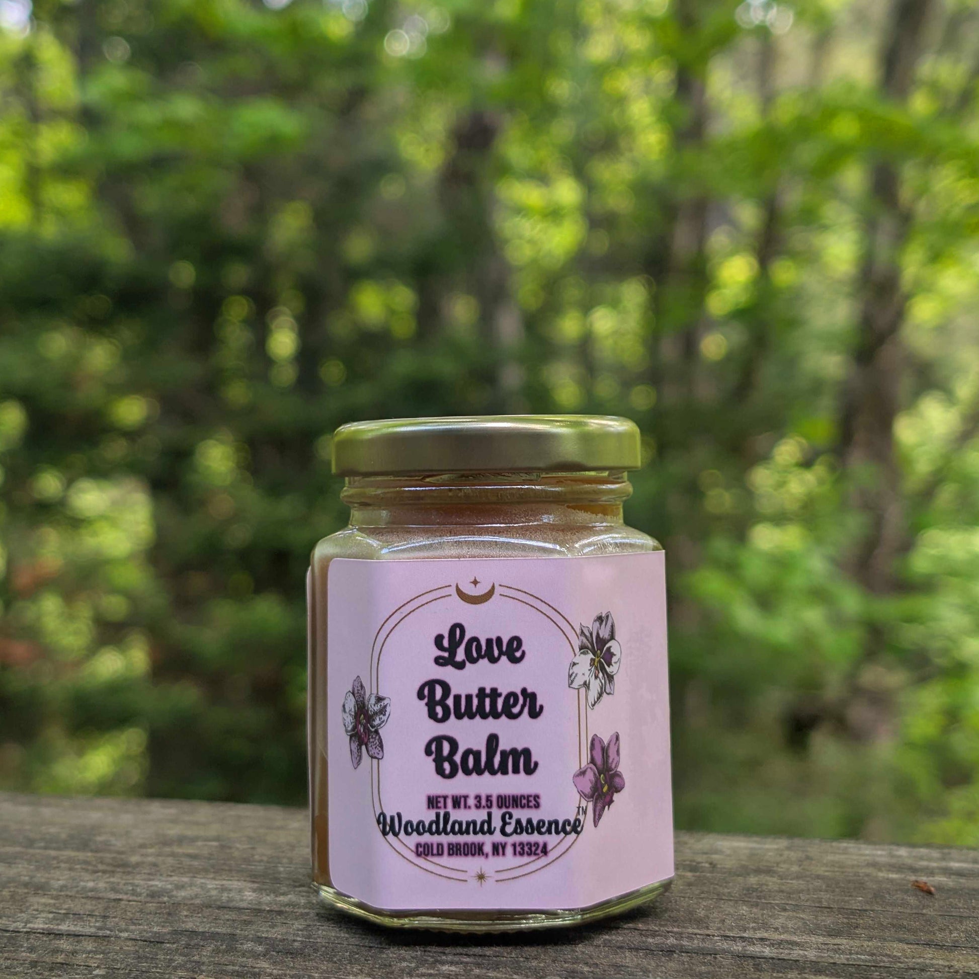 Jar of Love Butter Balm with a pink label against a blurred green forest background