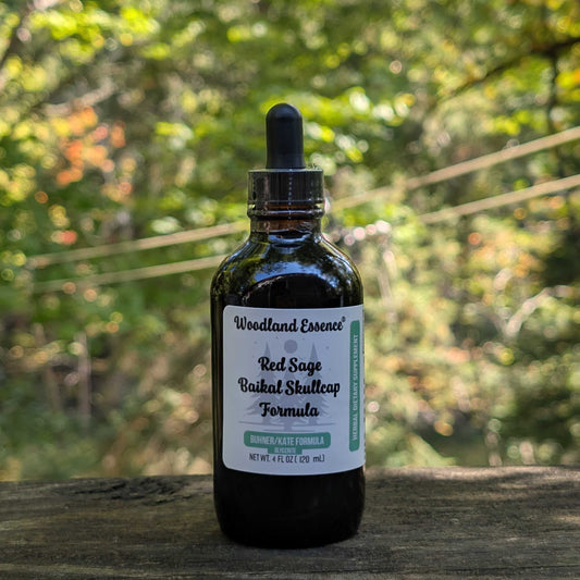 Bottle of Woodland Essence Red Sage Bakhai Skullcap Formula on a wooden surface with a blurred green background