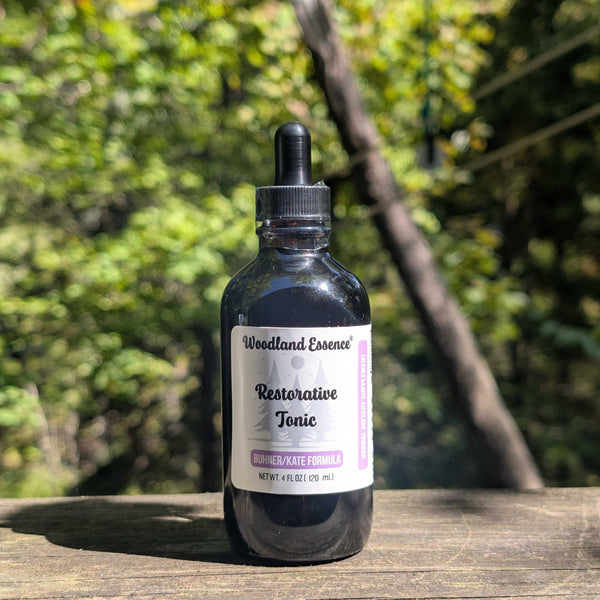 Bottle of Woodland Essence Restorative Tonic on a wooden surface with a blurred green background
